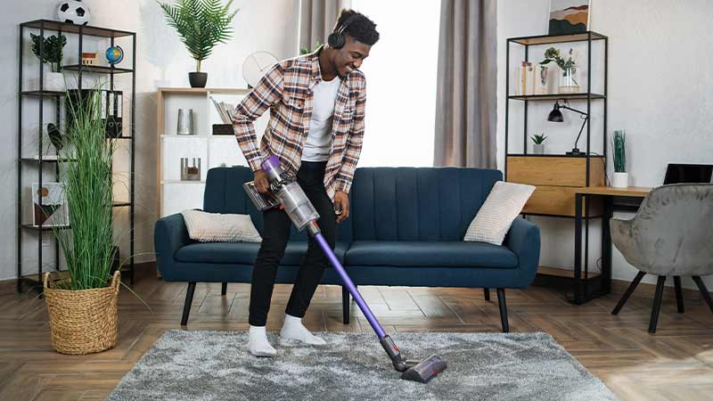 Homem jovem a aspirar o tapete da sala com um aspirador vertical sem fios